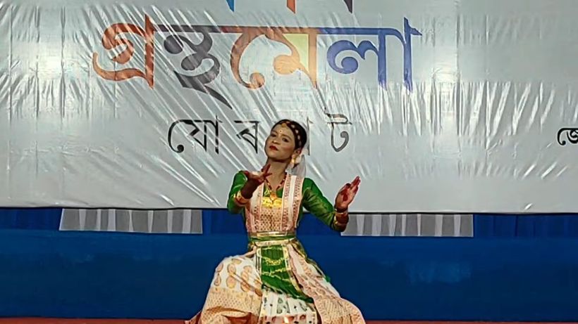 A student dancer in a green and gold costume mid-performance