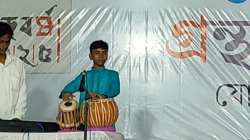A boy in a teal kurta playing the tabla