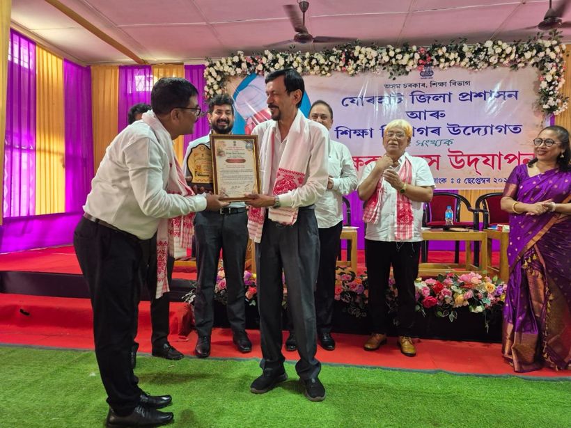 A teacher receives a framed certificate and a gamosa on stage at a Teachers’ Day celebration