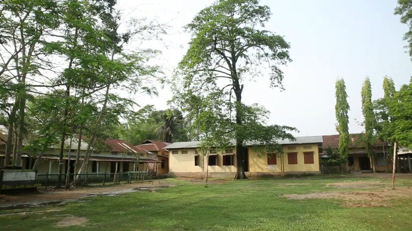 Trees and single-storey school buildings around a wide grass field