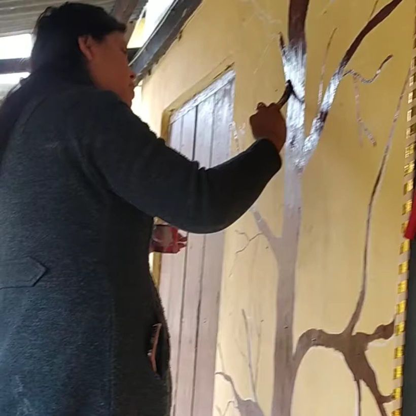 A teacher painting a tree on a yellow wall