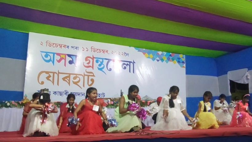 Young girls in party dresses seated on stage with pom-poms